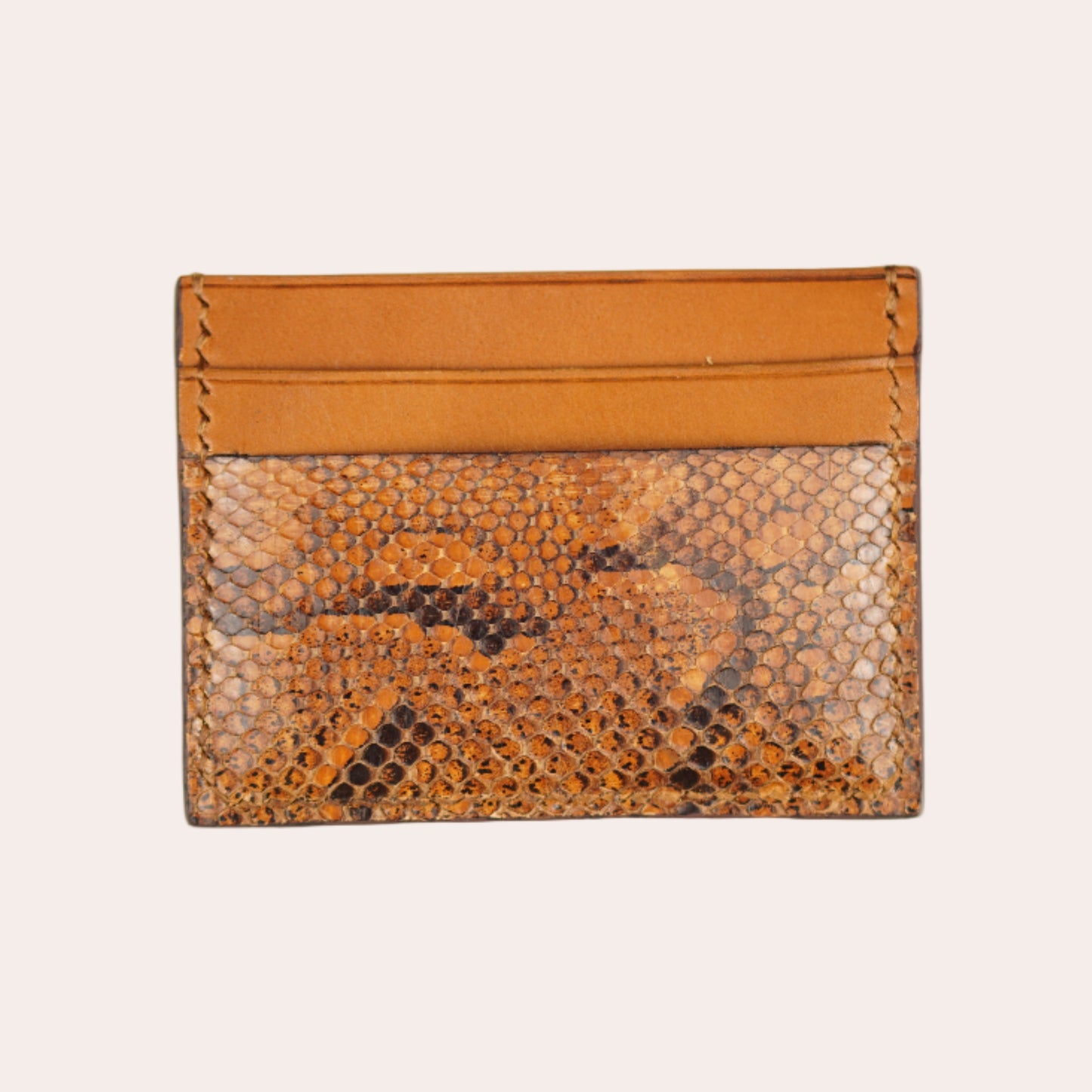 Snake skin patterned cardholder with orange top section on a beige background