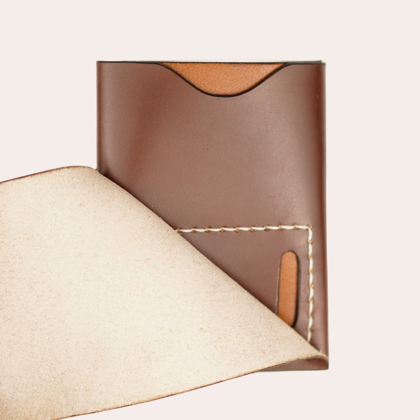 Brown leather wallet with beige interior held by a hand on a white background