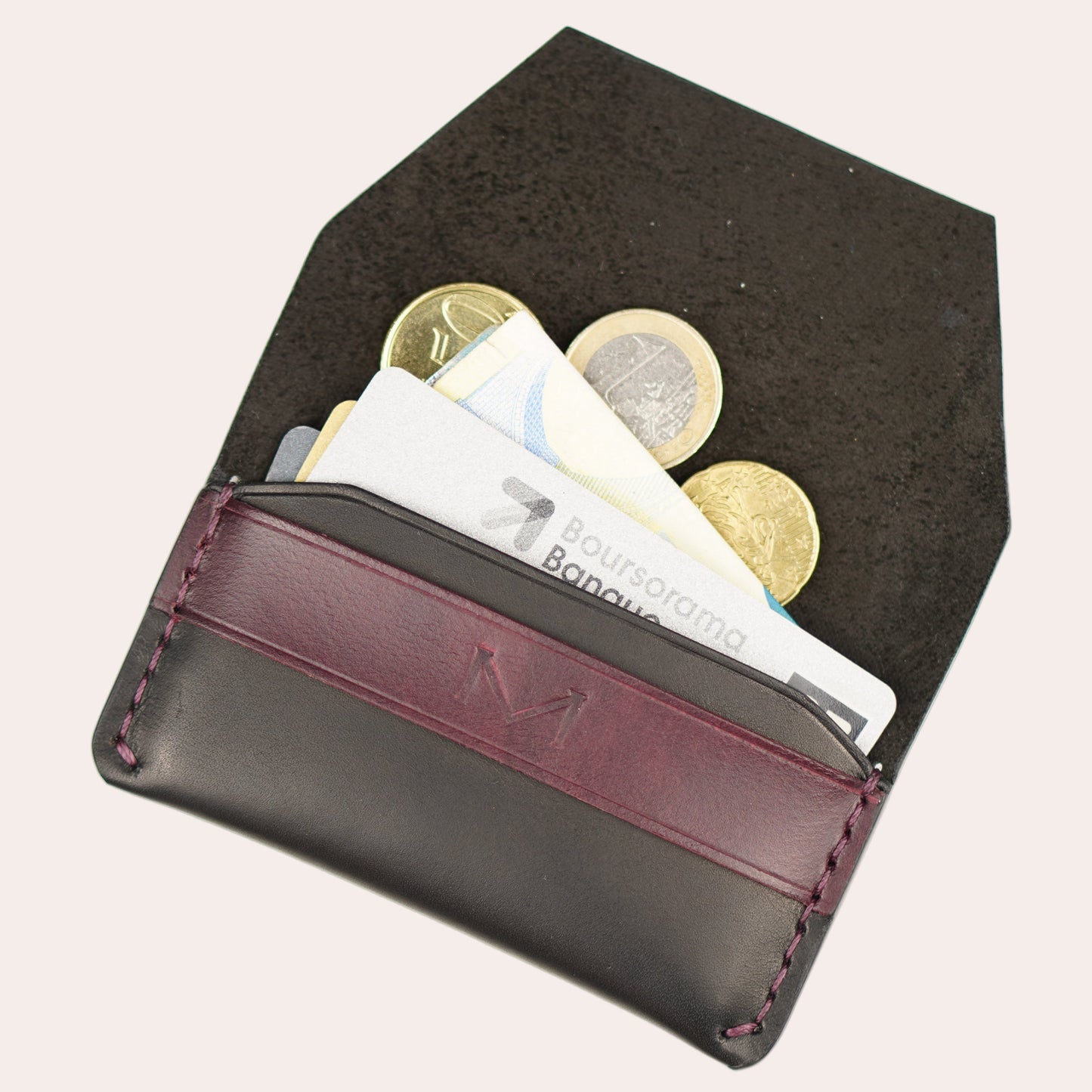 Black coin purse with a red strap holding coins and banknotes on a white background