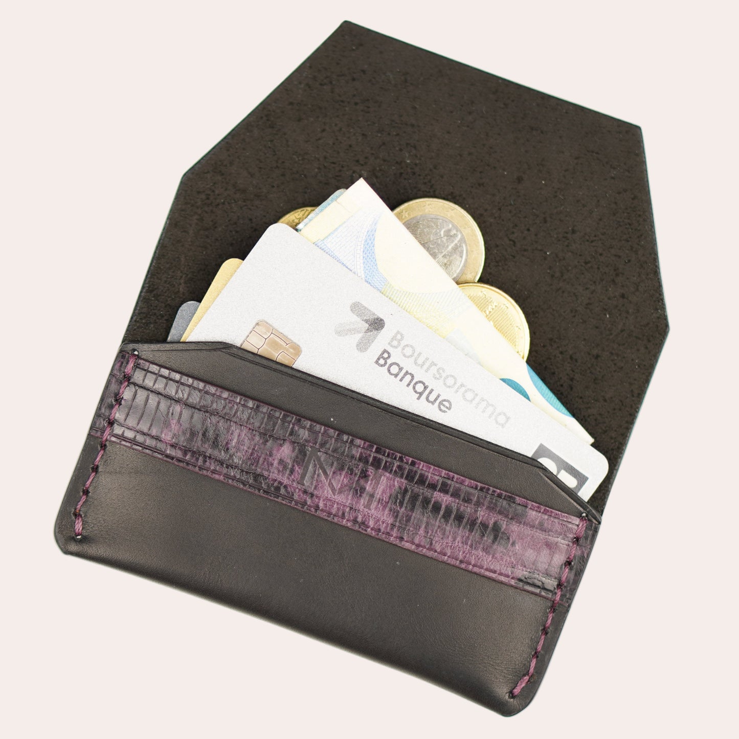Black wallet with purple interior lining containing money on a white background
