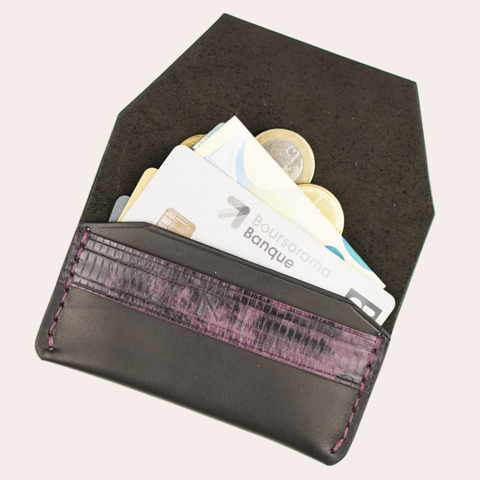 Black wallet with purple interior lining containing money on a white background