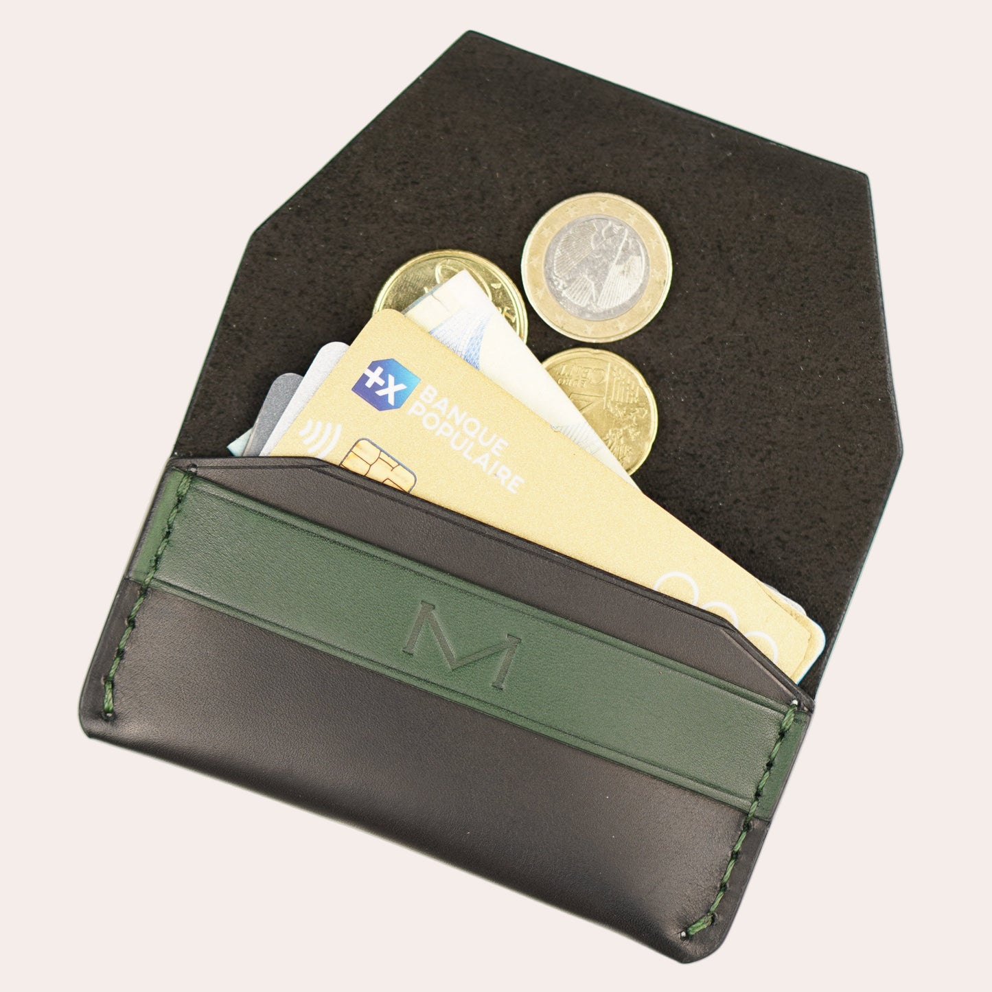 Black wallet with green strap holding cards and a coin on a white background