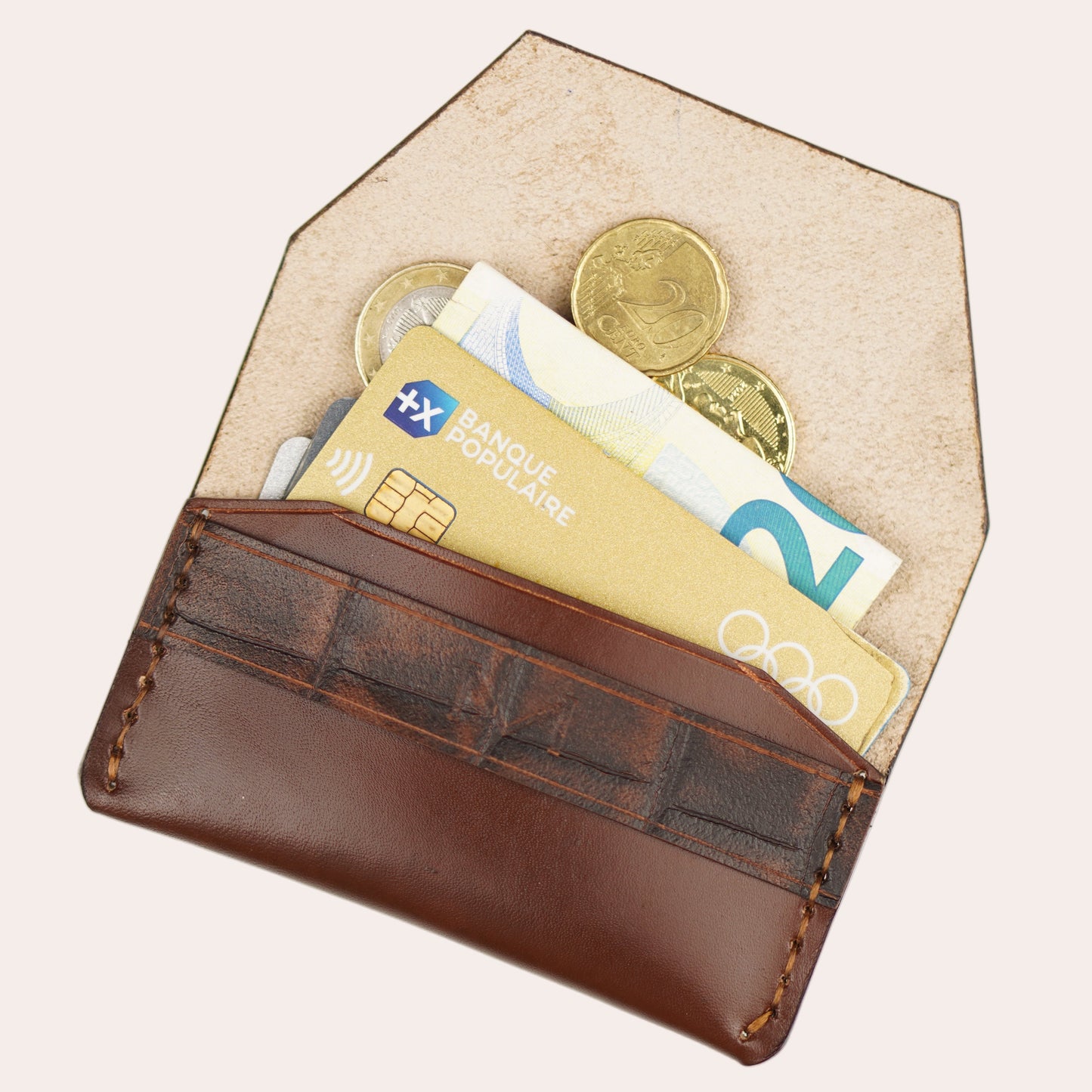 Brown leather wallet with beige interior holding money and coins on a white background