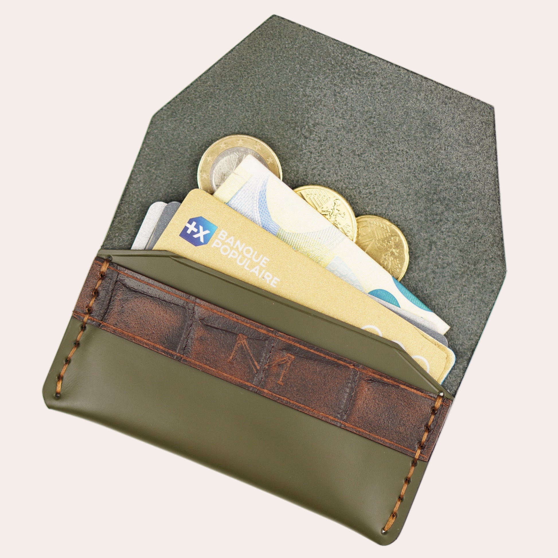 Green wallet with brown leather flap containing coins and cards on a white background